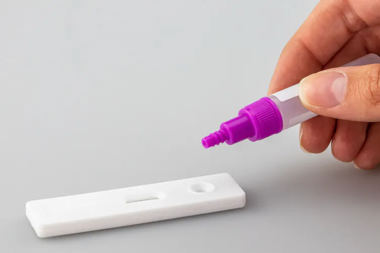 A hand dropping test solution onto a COVID-19 testing device.