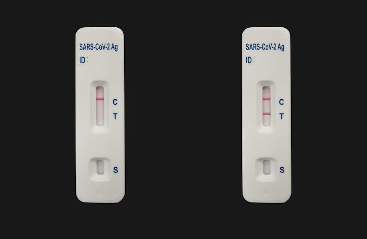 Two COVID-19 test devices, one with a negative reading and one positive, against a black background