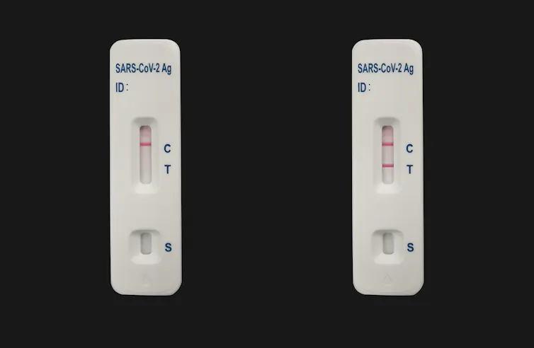 Two COVID-19 test devices, one with a negative reading and one positive, against a black background