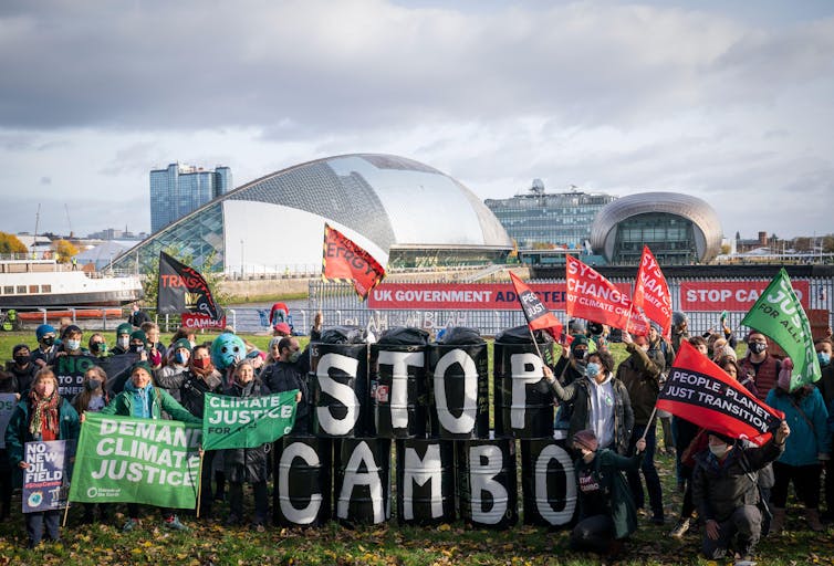 Activists hold flags and oil drums spelling 'Stop Cambo' outside the COP26 conference venue.