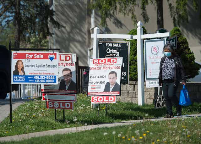 A woman wearing a surgical mask walks past several real estate signs