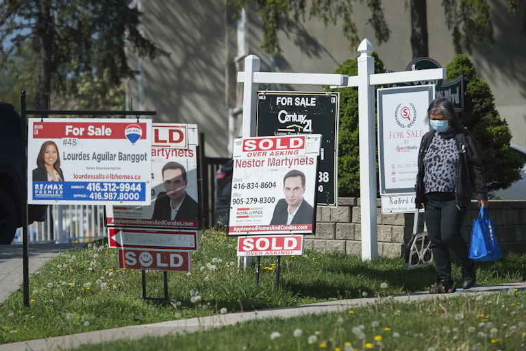 A woman wearing a surgical mask walks past several real estate signs