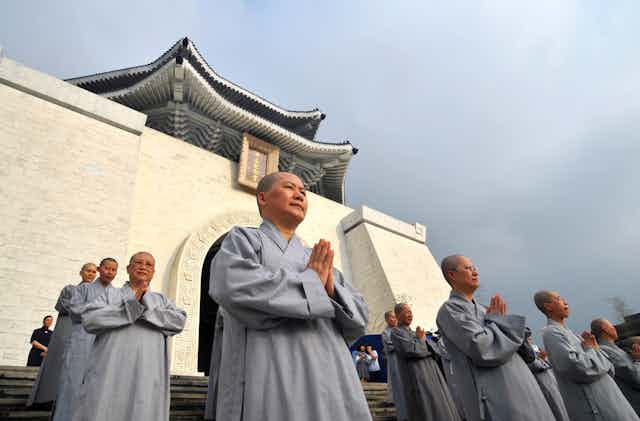 Nuns in gray robes pray in front of a Buddhist temple.
