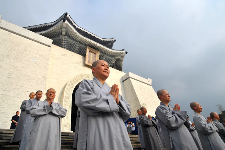 Nuns in gray robes pray in front of a Buddhist temple.