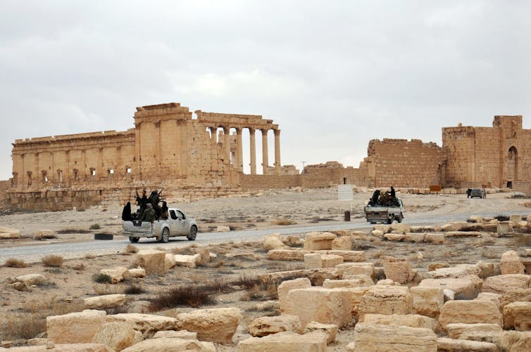 soldiers with guns ride in pickup trucks through ancient city of Palmyra