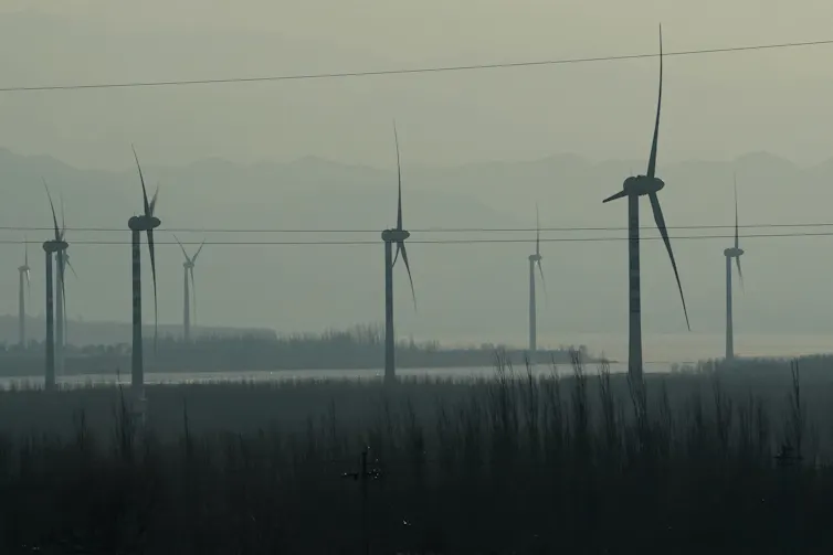Wind turbines rise over fields in a hazy atmosphere.