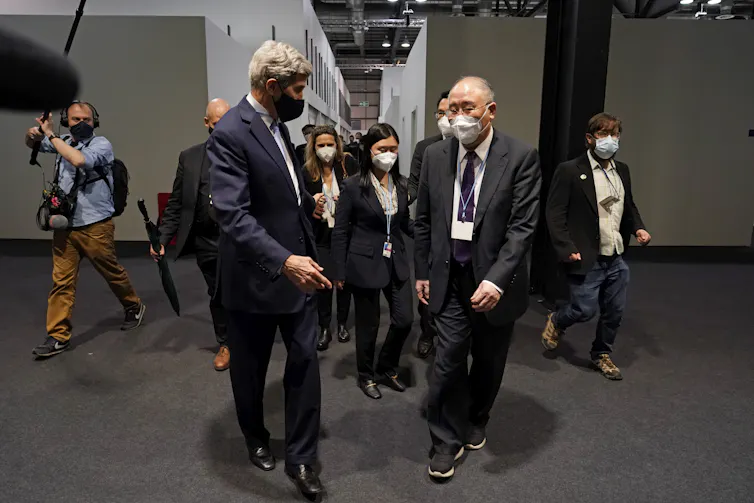 Two men walk down a hallway trailed by staffers and media.