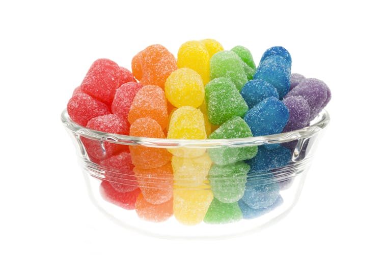 Rainbow-colored gum drops in a glass bowl against a white background.
