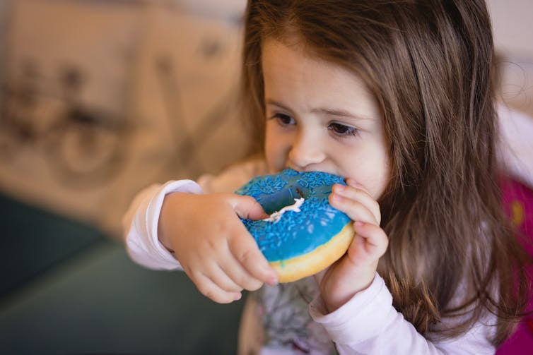 Child eating a donut with blue frosting.