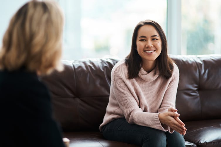 A young woman sits on a couch facing another woman.