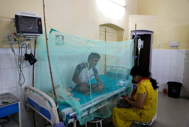 Man on hospital bed inside mosquito netting