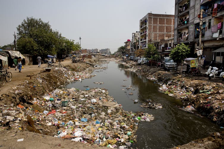 A stagnant river with rubbish surrounding the banks.