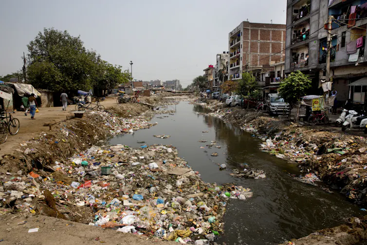 A stagnant river with rubbish surrounding the banks.