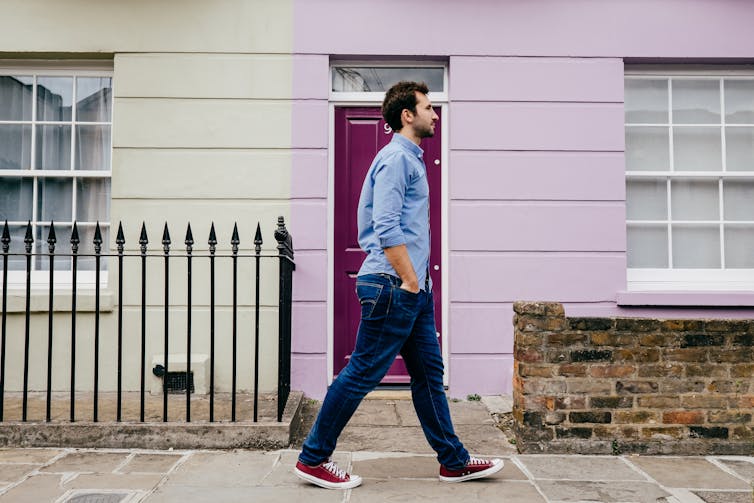 Young man walks in front of a purple house.