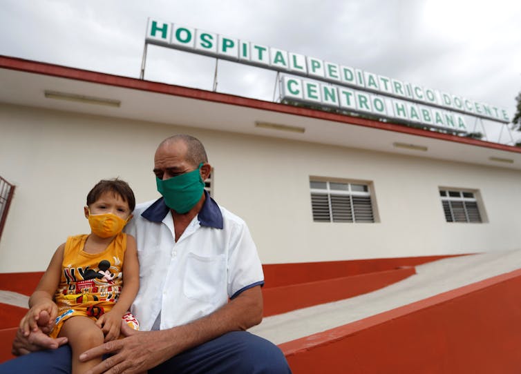 Ένας άντρας που κρατά τον γιο του έξω από ένα παιδιατρικό νοσοκομείο στην Αβάνα της Κούβας