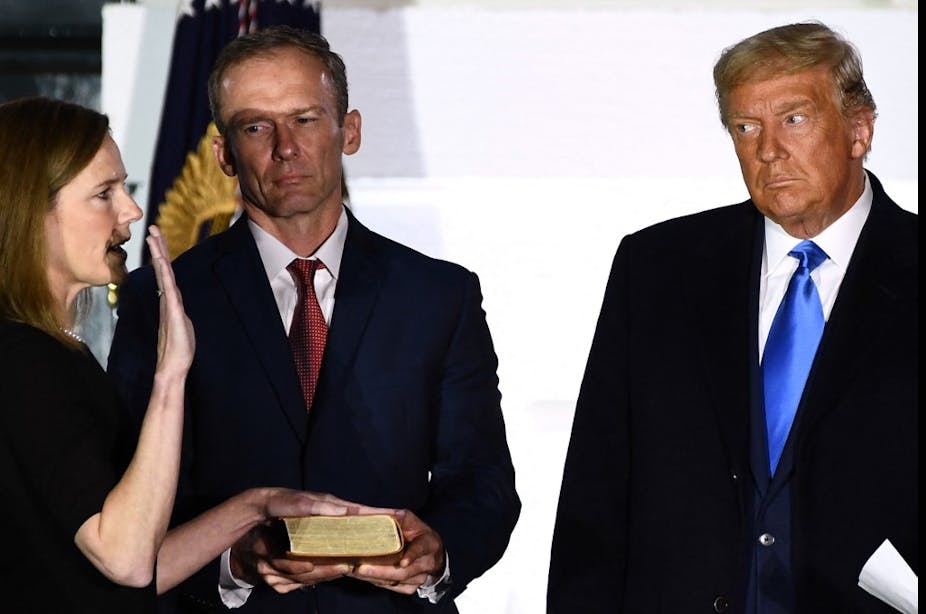 Donald Trump et un autre homme en costume regardent une femme prêter serment la main posée sur un livre.