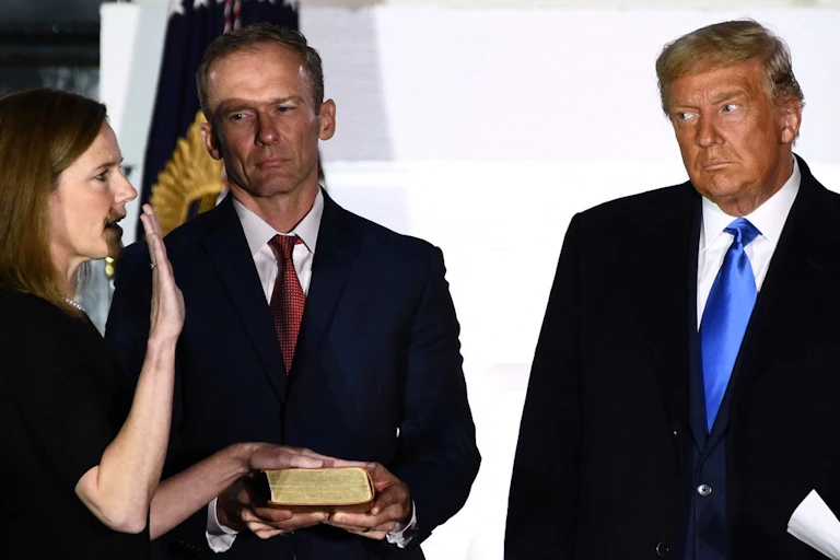 Donald Trump et un autre homme en costume regardent une femme prêter serment la main posée sur un livre.