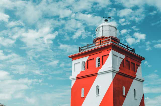 A red and white lighthouse set against a cloudy blue sky.