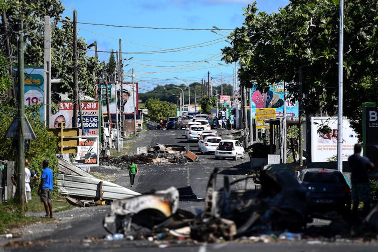 Un piéton traverse un barrage filtrant fait de véhicules brûlés et de débris à Mare Gaillard, près de Pointe-a-Pitre la Guadeloupe, le 22 novembre 2021