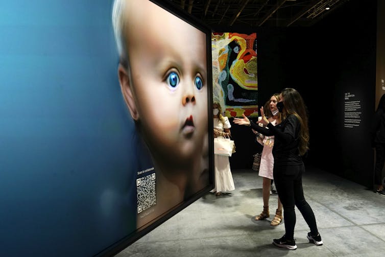 People look at a digital piece of art of a blue-eyed baby.