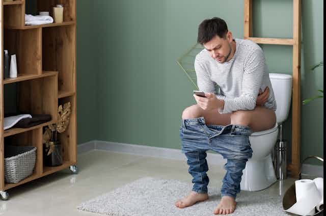 A man sitting on the toilet on his phone.