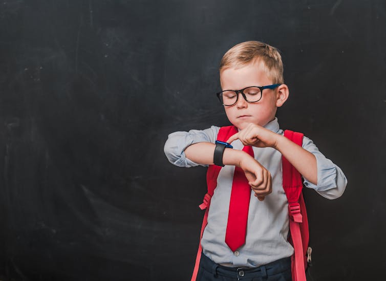 A young boy wearing a red backpack looks at his smartwatch