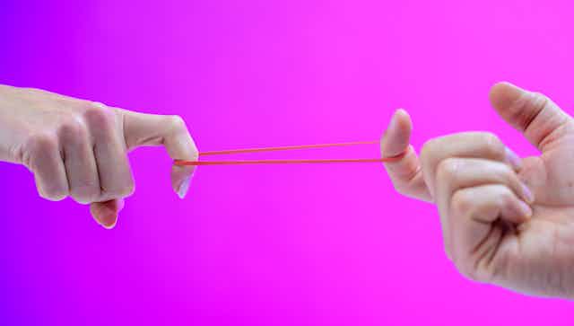 Close-up photo of a male and female hand stretching a rubber band between their index fingers.