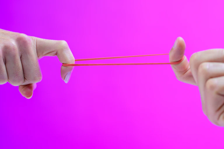 Close-up photo of a male and female hand stretching a rubber band between their index fingers.