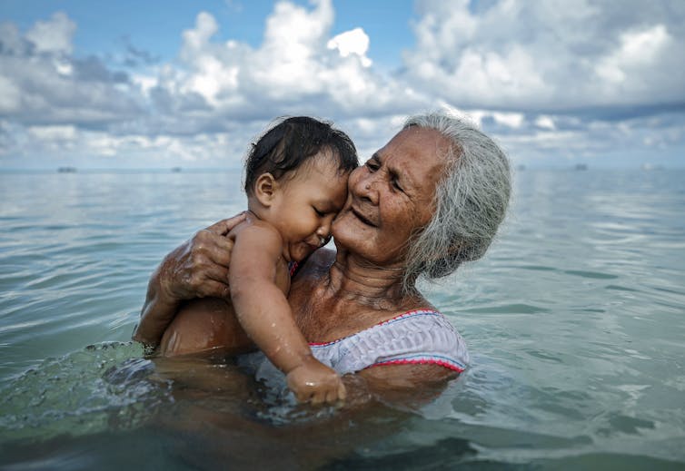 A elder bathes a young child in a lagoon in Tuvalu.