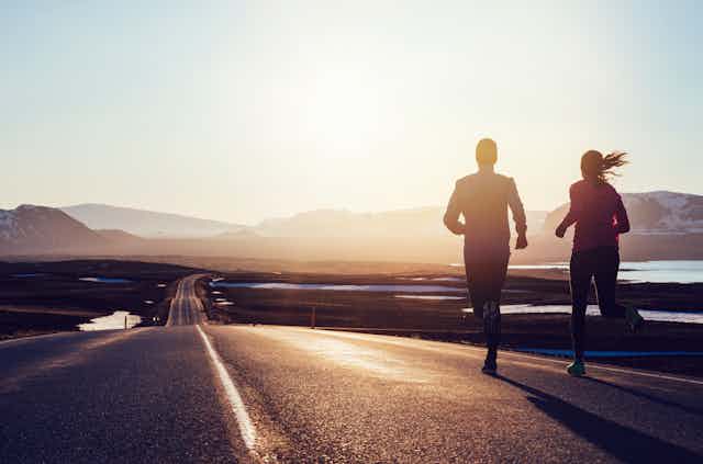 Two runners jogging together on the side of a road.