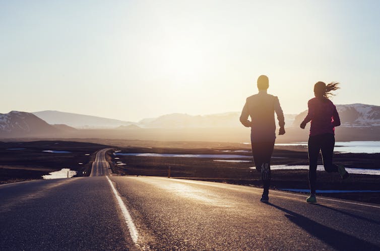 two runners on road facing a sunset