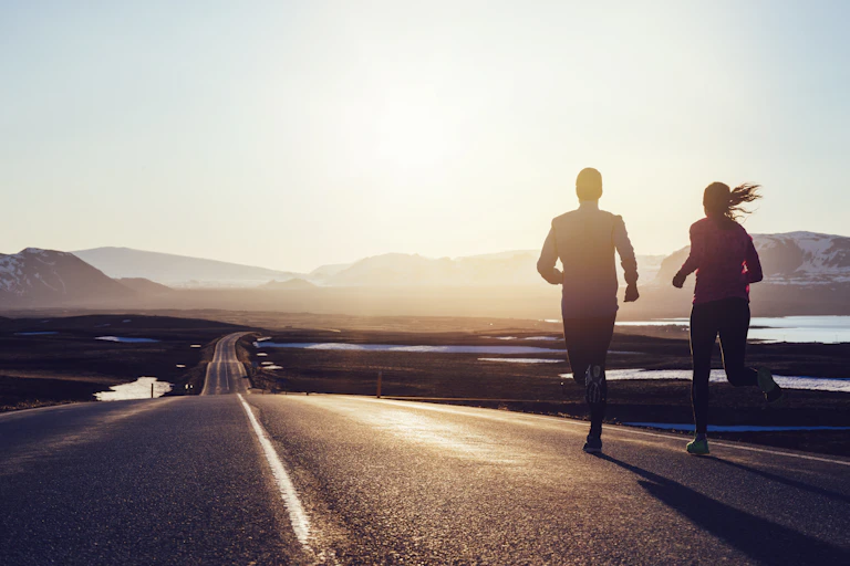 Two runners jogging together on the side of a road.