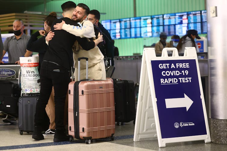 People embrace next to a free COVID-19 rapid testing sign at Los Angeles International Airport.