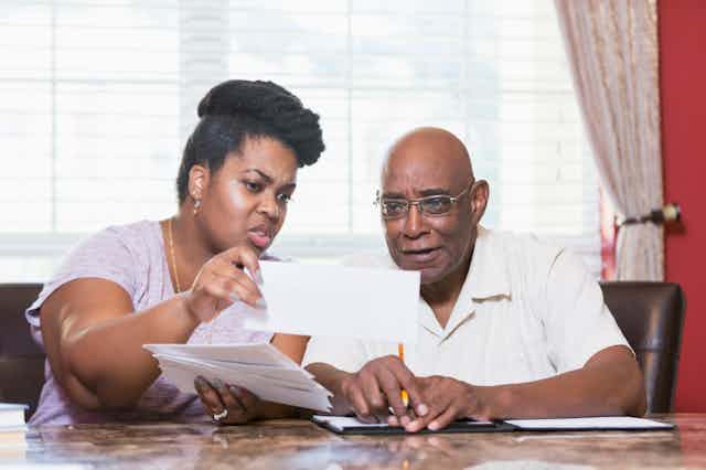 A middle-aged Black couple reviews paperwork at a desk.