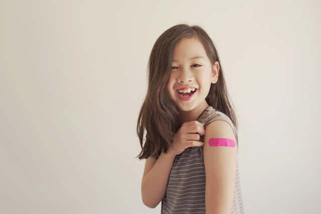 Young girl shows her bandaid after being vaccinated.