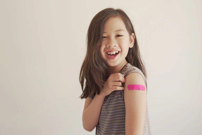 Young girl shows her bandaid after being vaccinated.