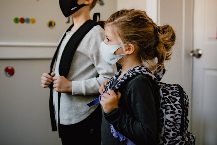 Two children in masks wait by a door.