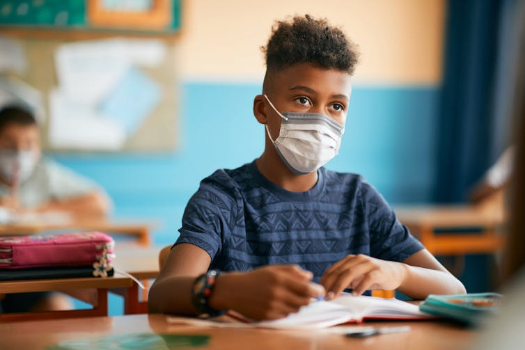 Boy in a mask sits in a classroom.