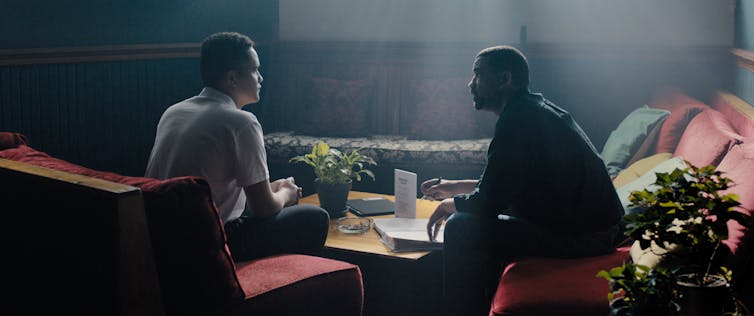 Two men sit in a room and talk
