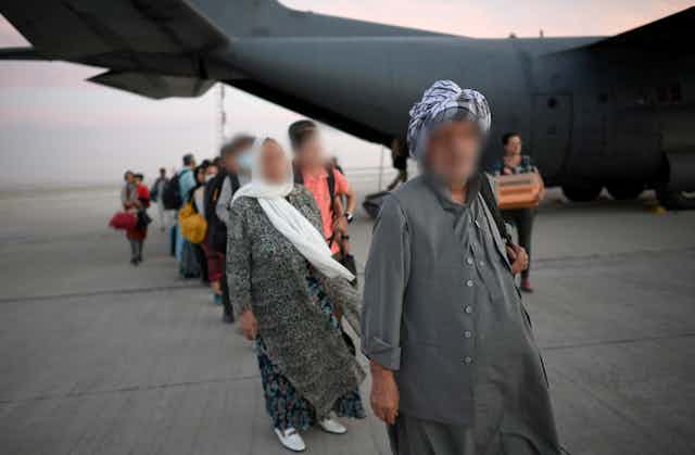 A queue of people with their faces blurred in front of a large military plane