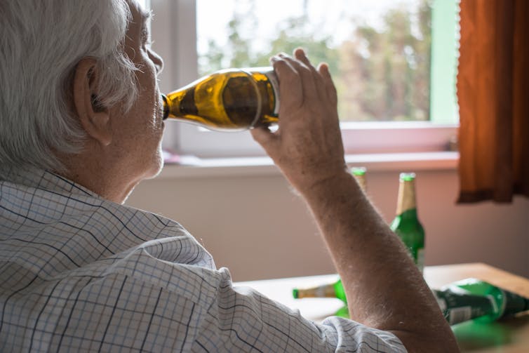 Older man drinking a bottle of beer in his home.