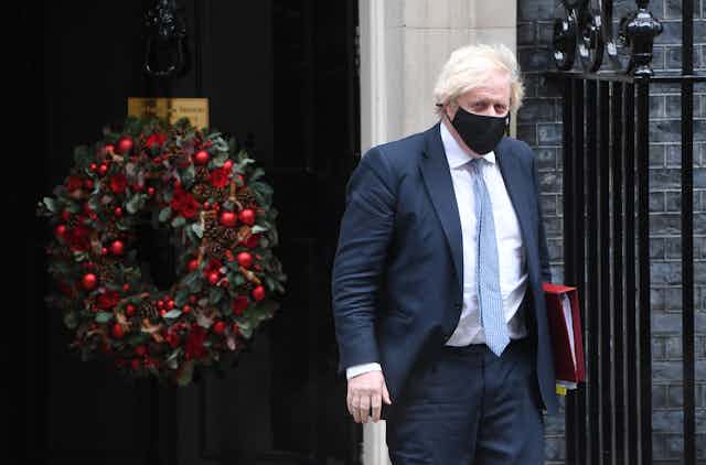 Boris Johnson walking out of 10 Downing Street with a large Christmas wreath on the door behind him. 