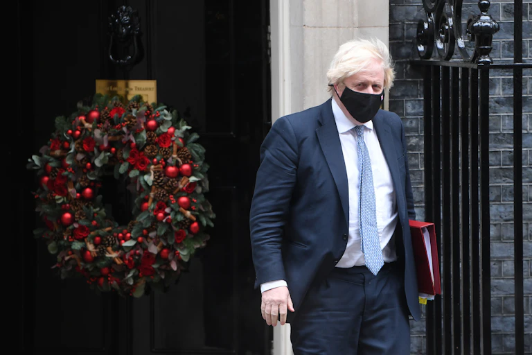 Boris Johnson walking out of 10 Downing Street with a large Christmas wreath on the door behind him.