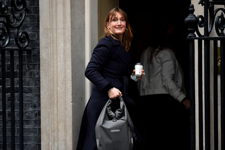 Allegra Stratton smiles for the camera as she walks into 10 Downing Street with a coffee.