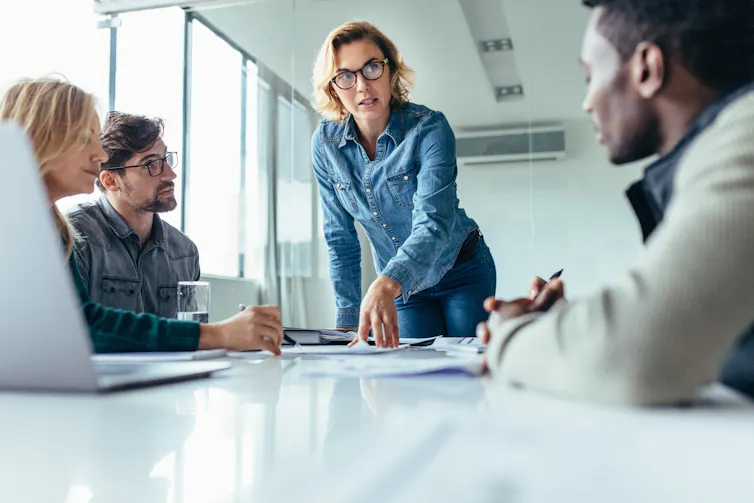 A woman talks to a group of employees at a boardroom table.