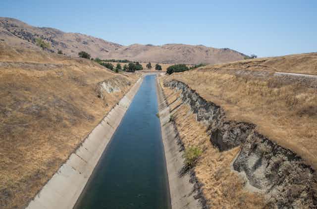 A cement canal carrying water through a dry landscape