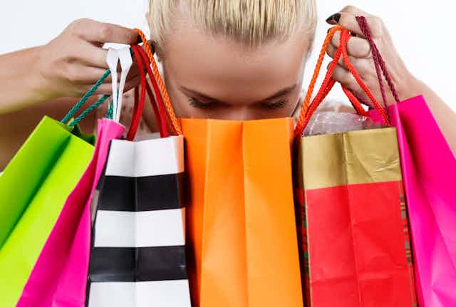 A blonde woman holds six shopping bags in her hands and peers into them.