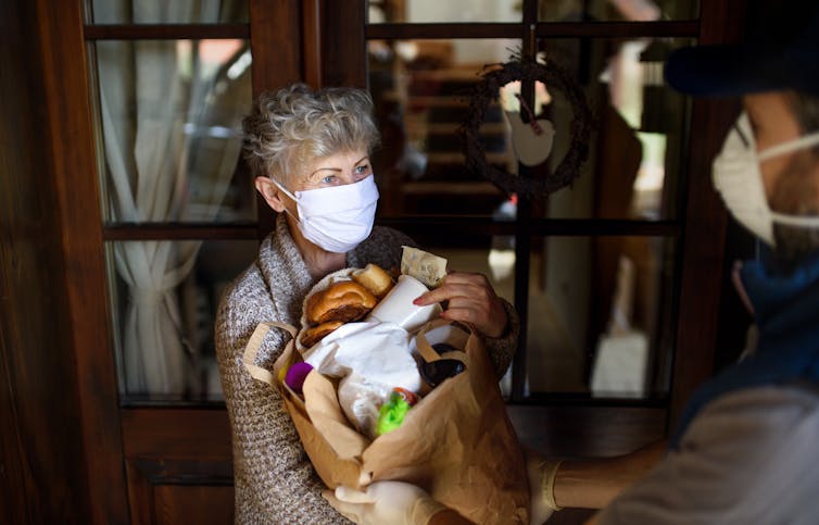 Courier delivering shopping to an elderly woman with face mask.