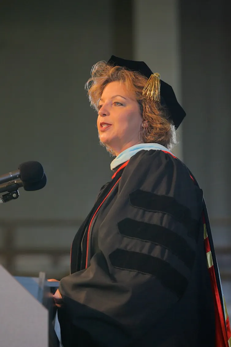A woman in graduation regalia speaking to an audience.