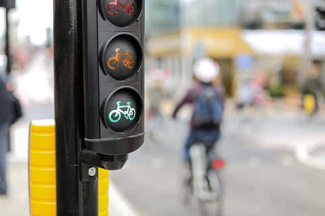 A traffic light with a green bike highlighted in foreground, a cyclist out of focus in background.